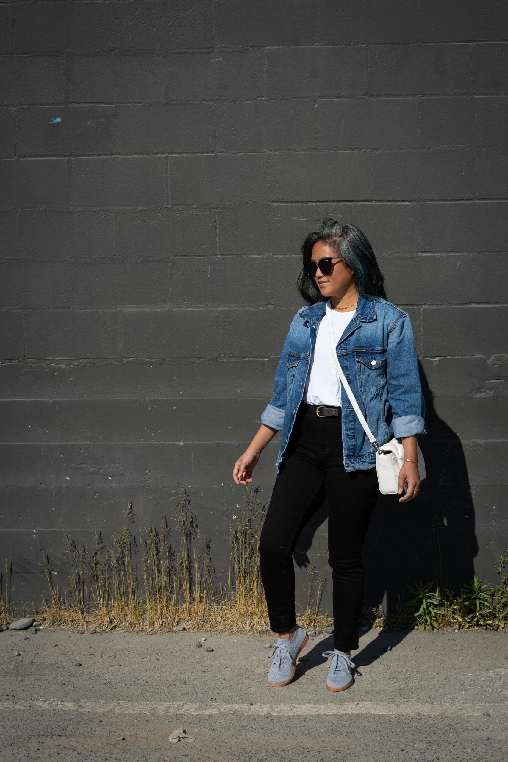 woman in blue denim jacket and black pants standing beside gray wall